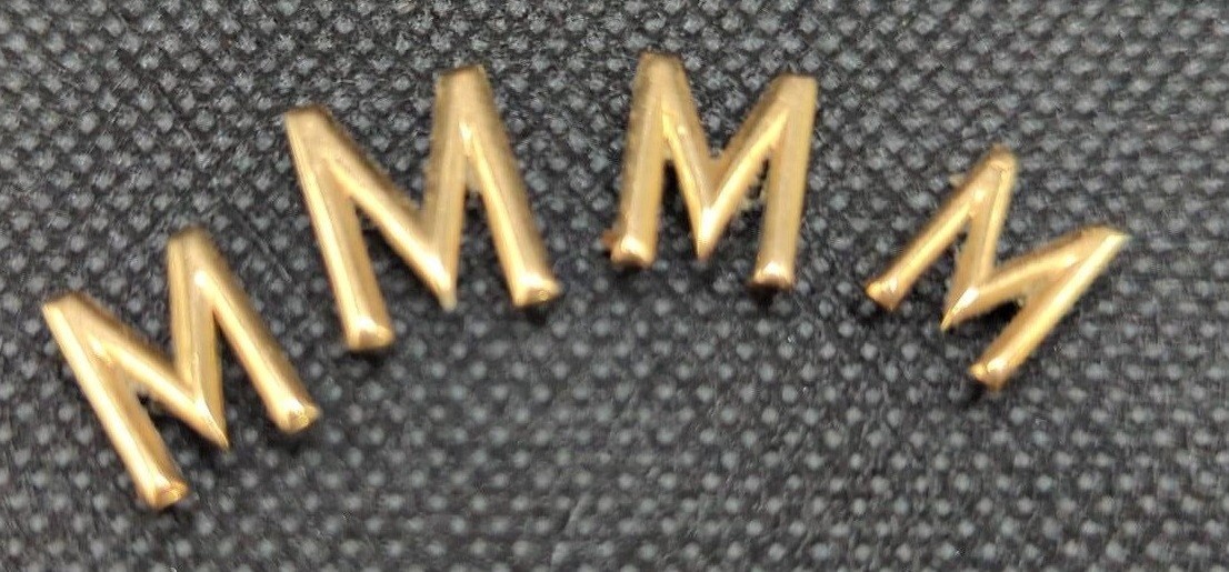 Four yellow metal letter 'M' appliques, gross weight 2.4 grams.